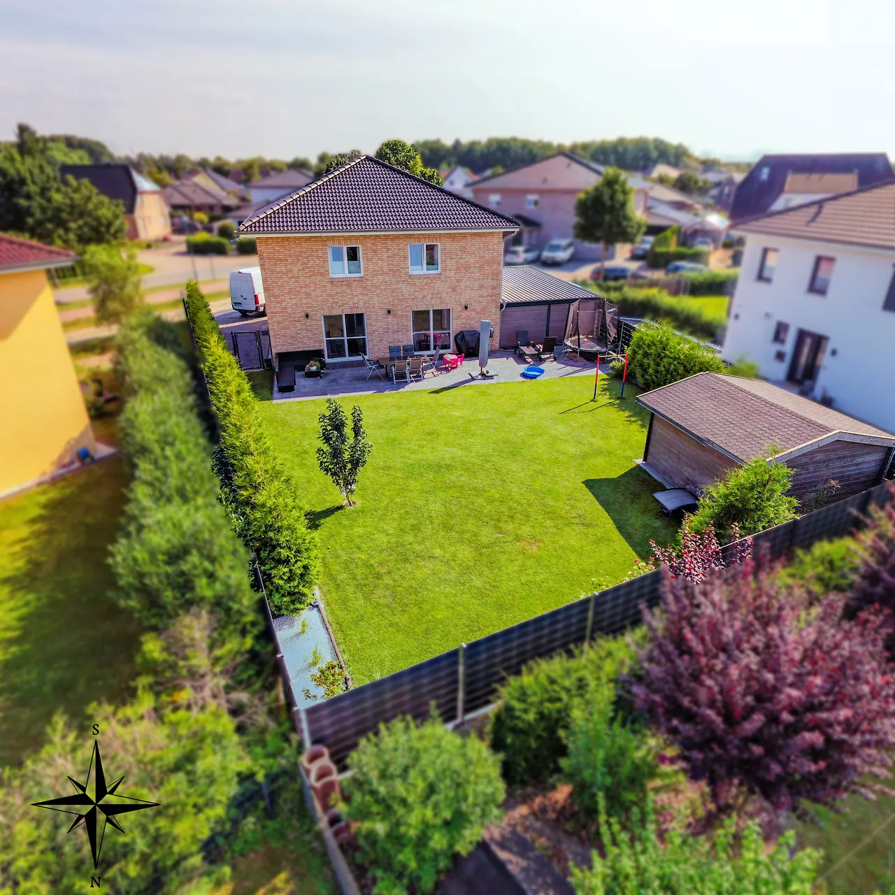 Einfamilienhaus mit Terrasse und großem Garten aus der Vogelperspektive, mit Kompassrose zur Ausrichtung