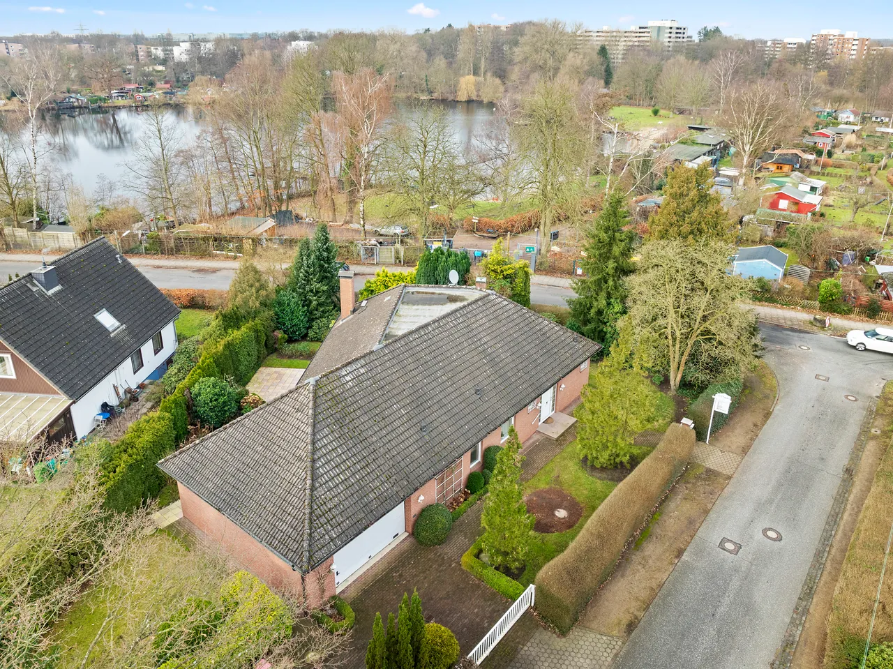 Einfamilienhaus mit Walmdach und Garten, dahinter ein See und Kleingärten – Luftaufnahme